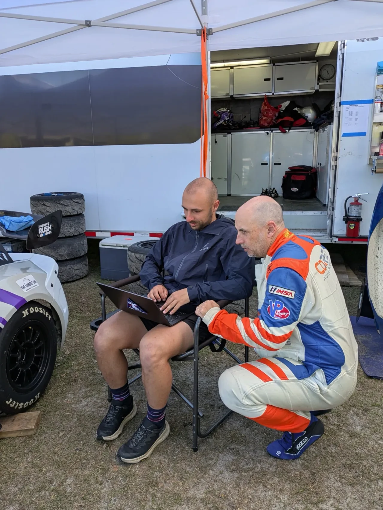 Driver and crew member reviewing a laptop beside the race car in the paddock